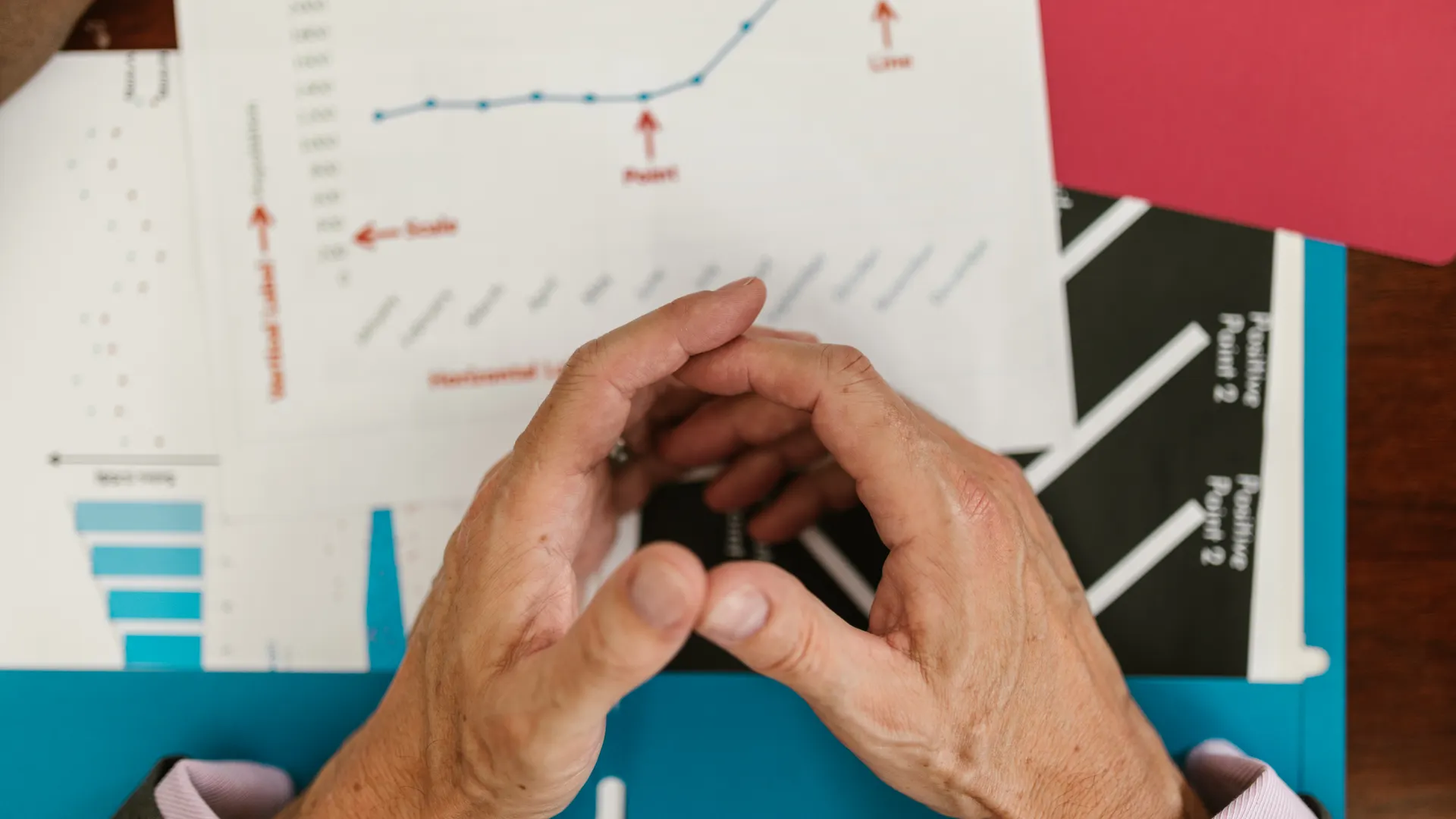 Hands examining financial graphs and charts on a wooden desk, indicative of business planning