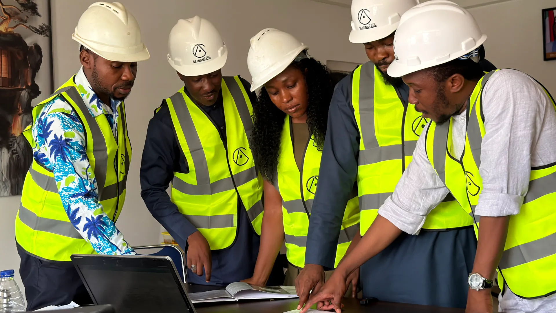Group of engineers in safety gear reviewing blueprints indoors