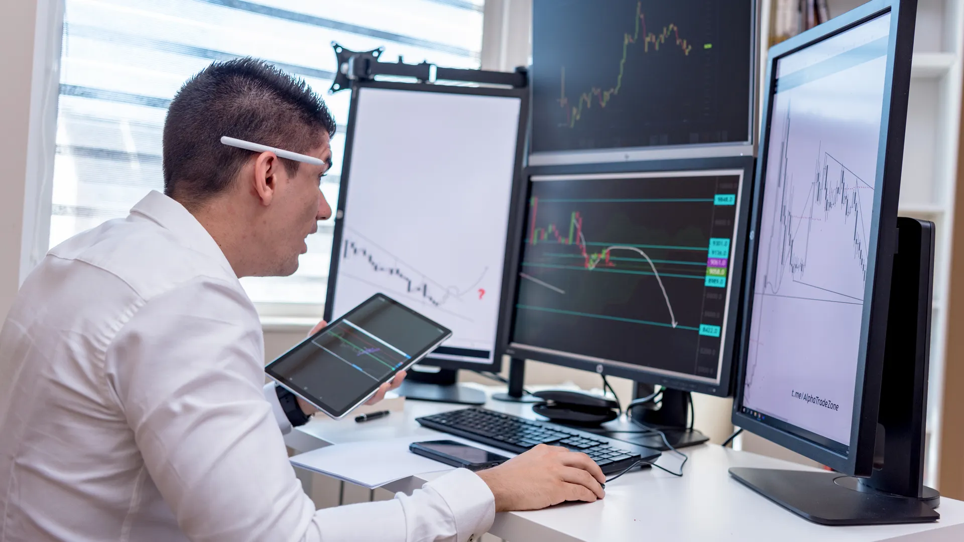 A man analyzing stock market graphs on multiple screens at a workstation