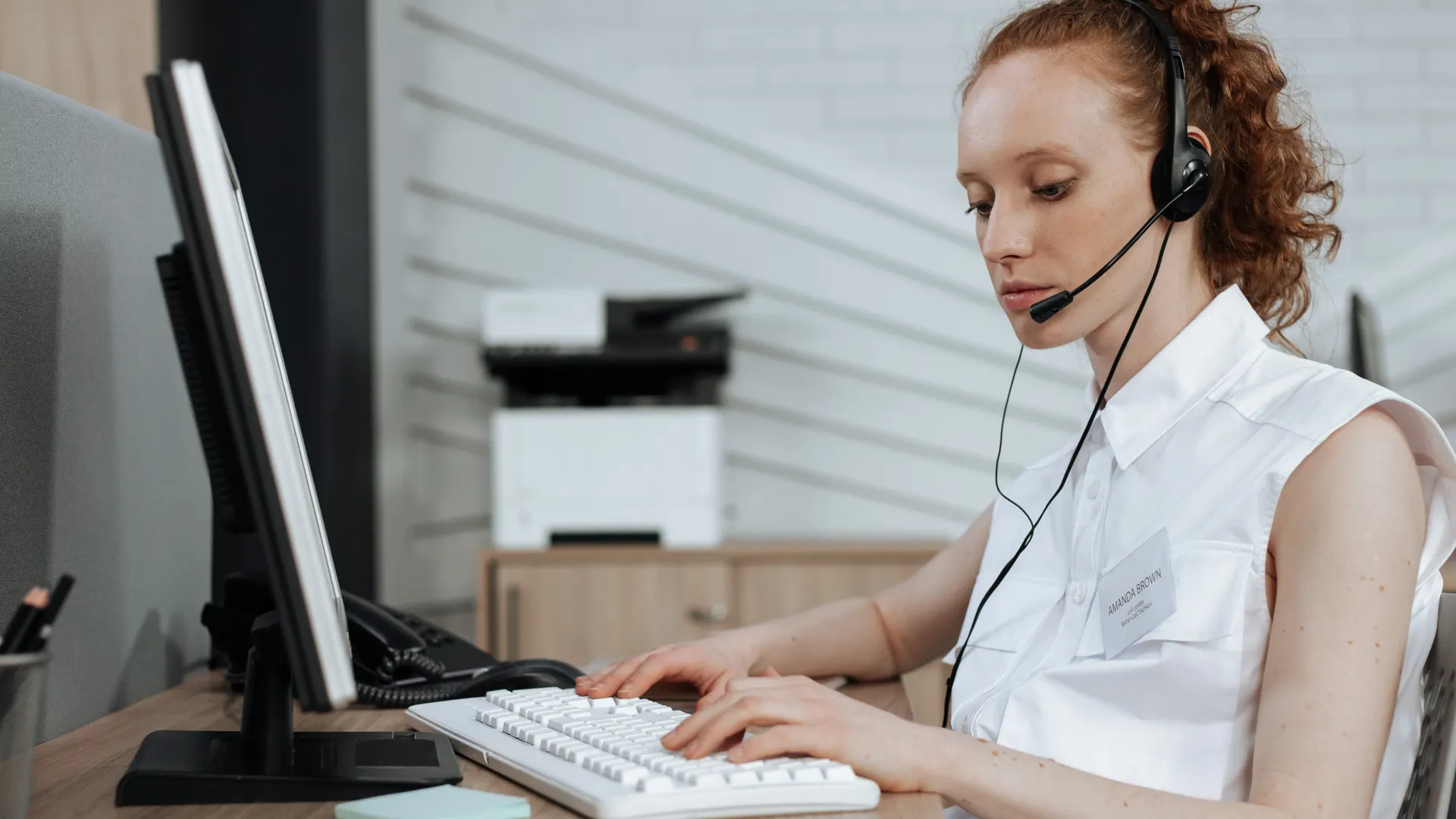 A female call center agent typing on a keyboard while wearing a headset at her desk