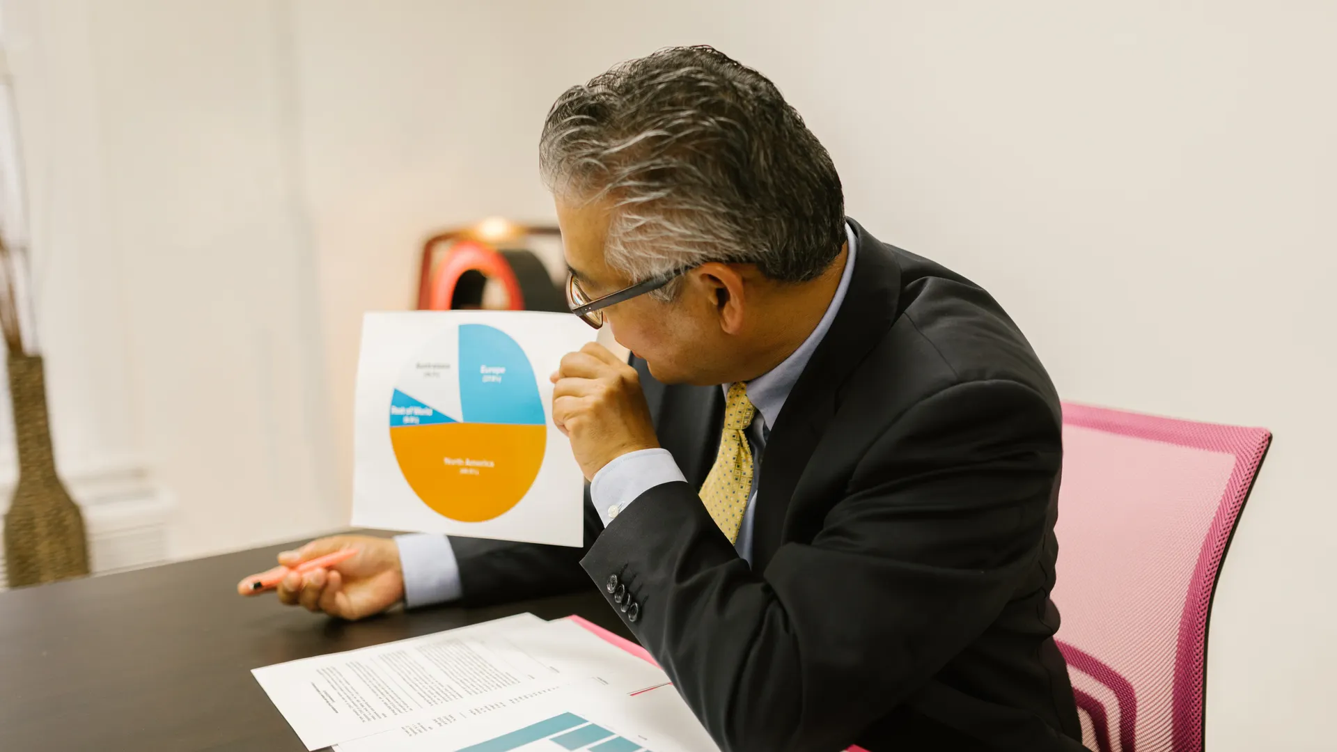 A businessman in a suit reviews pie chart documents at his office desk