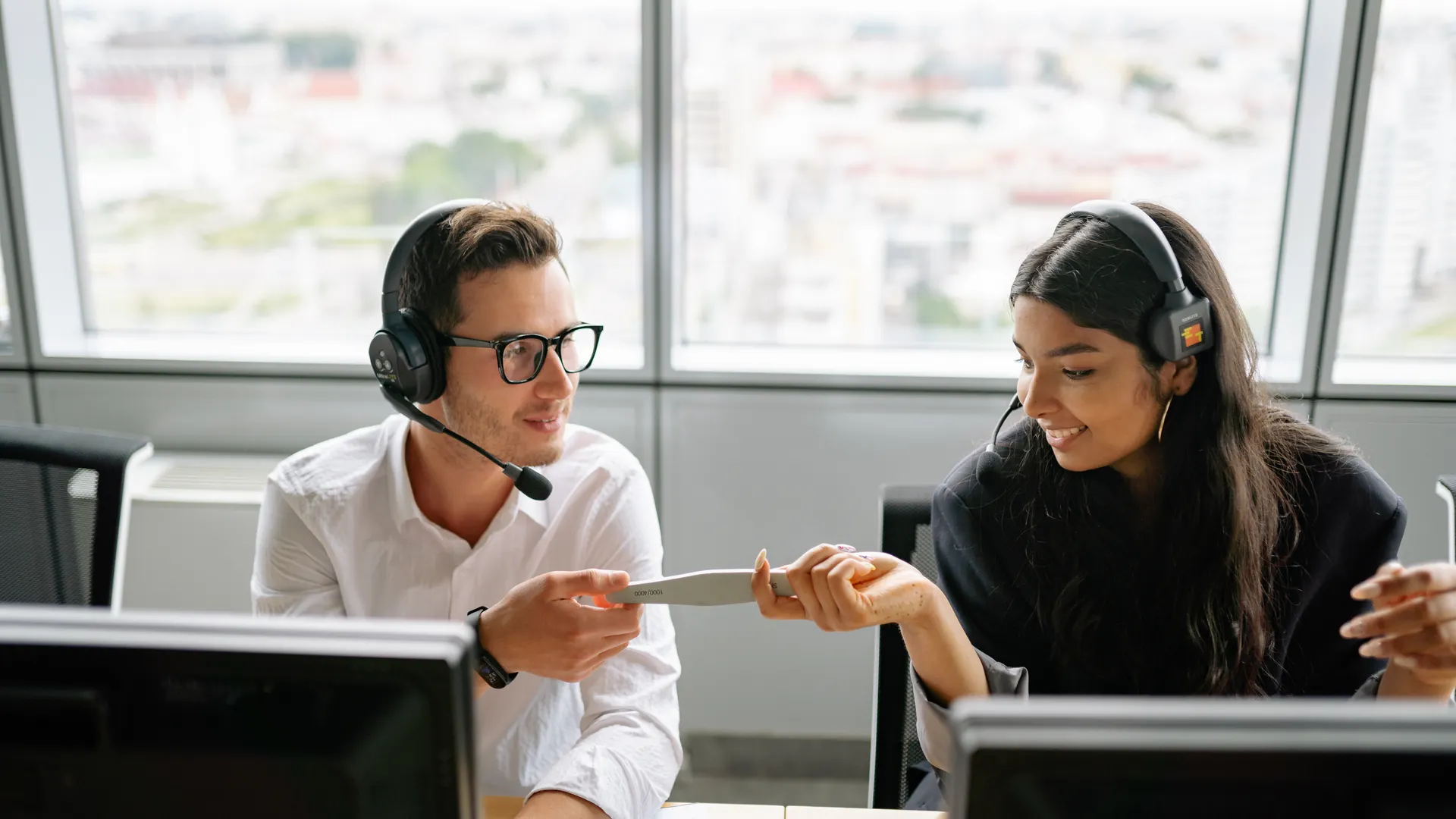 Two call center agents sharing a document while communicating with clients, fostering teamwork