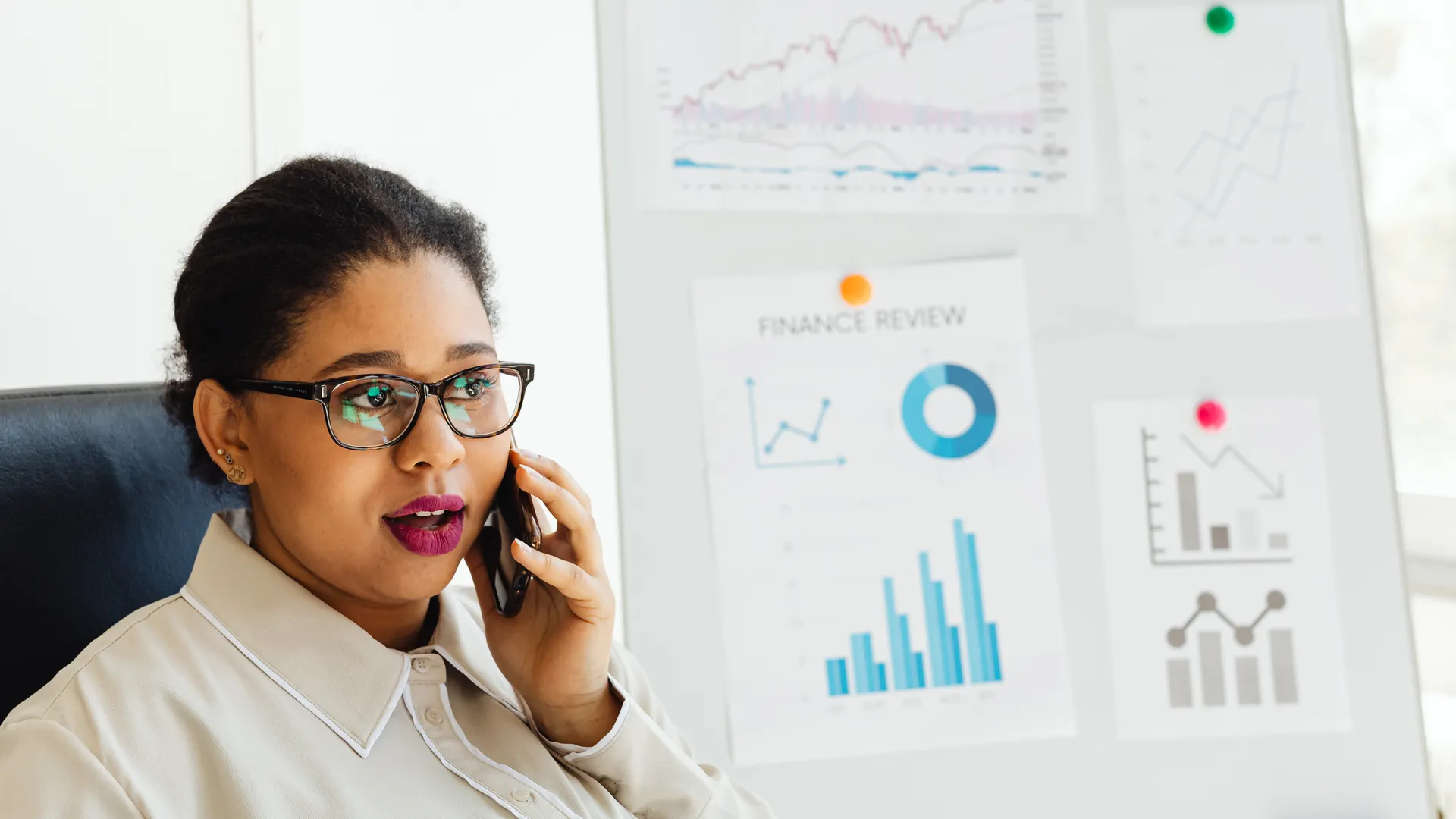 Focused businesswoman on call analyzing financial data displayed on whiteboard charts