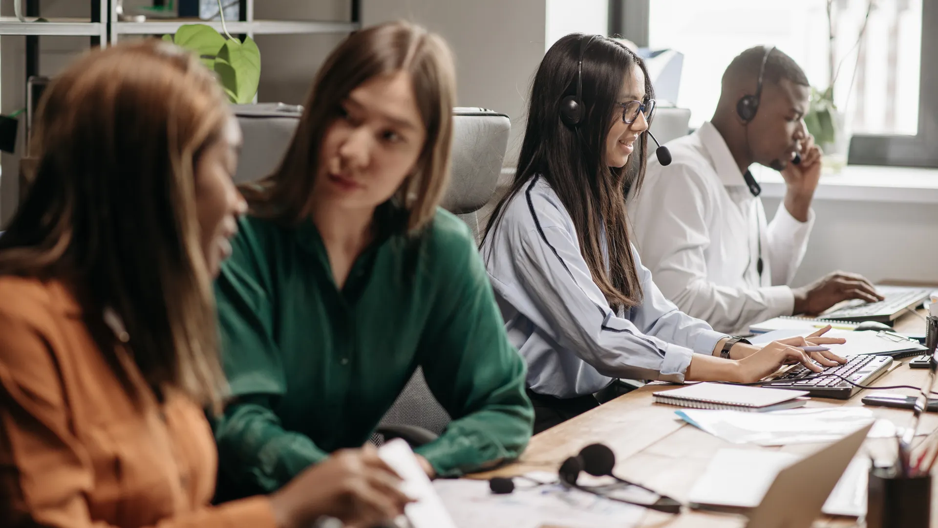 A diverse group of call center employees collaborating with headsets and computers