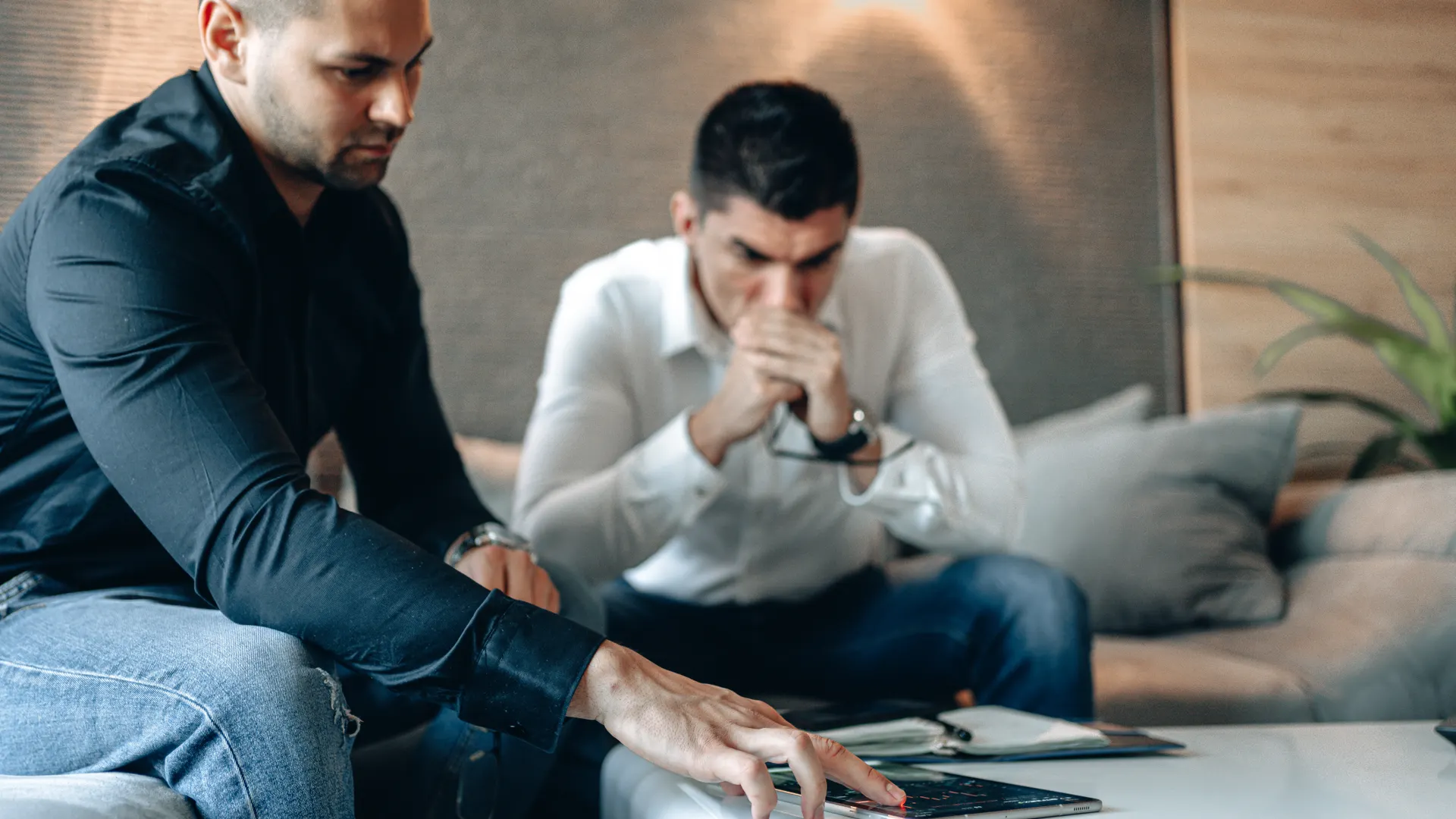 Two men engaged in a serious discussion, analyzing cryptocurrency data on a tablet indoors