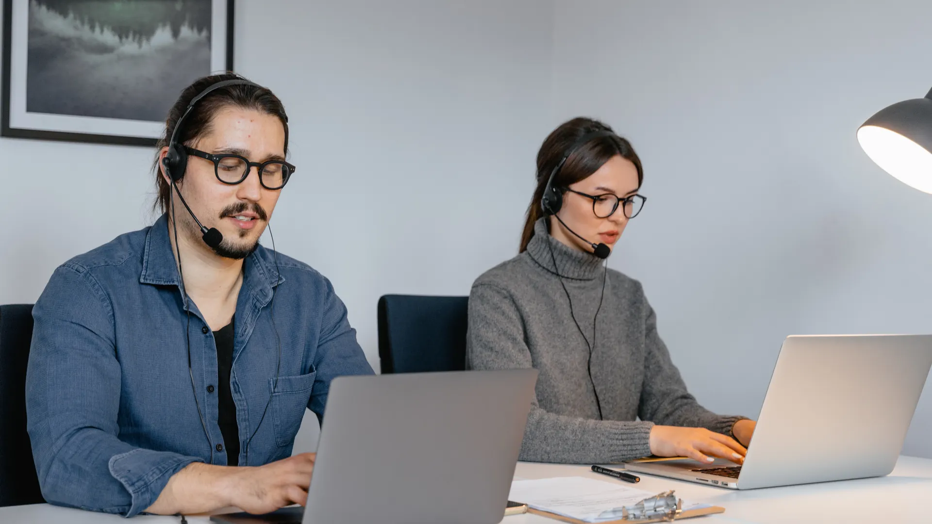 Two focused call center agents working on laptops with headsets in an office setting