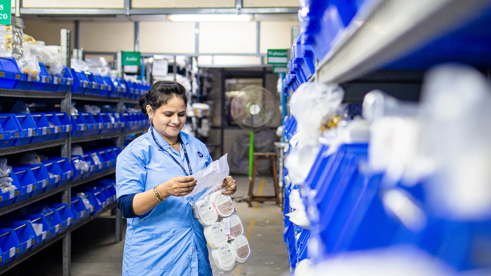A woman in blue uniform organizing inventory in a warehouse aisle, focused on efficiency