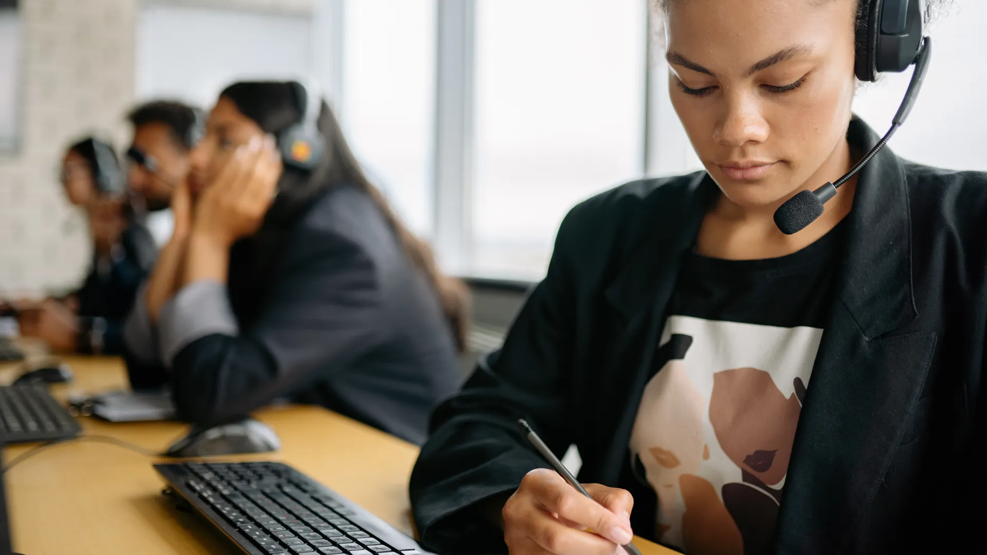 Focused call center employee using headset and writing notes at her desk, working efficiently