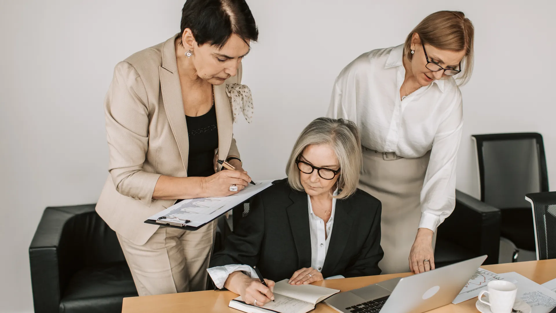 Three professional women collaborating in a business meeting with documents and laptops