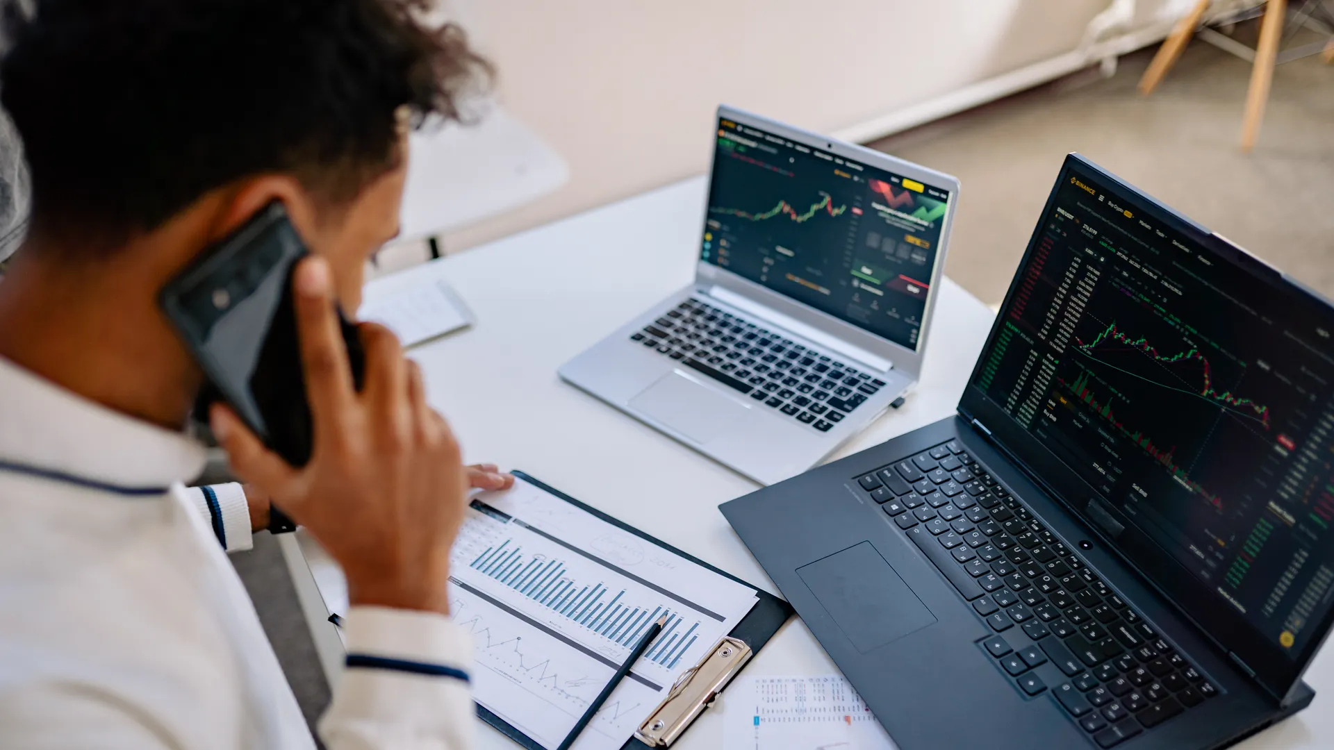 Man analyzing stock market charts on laptops while talking on a cellphone